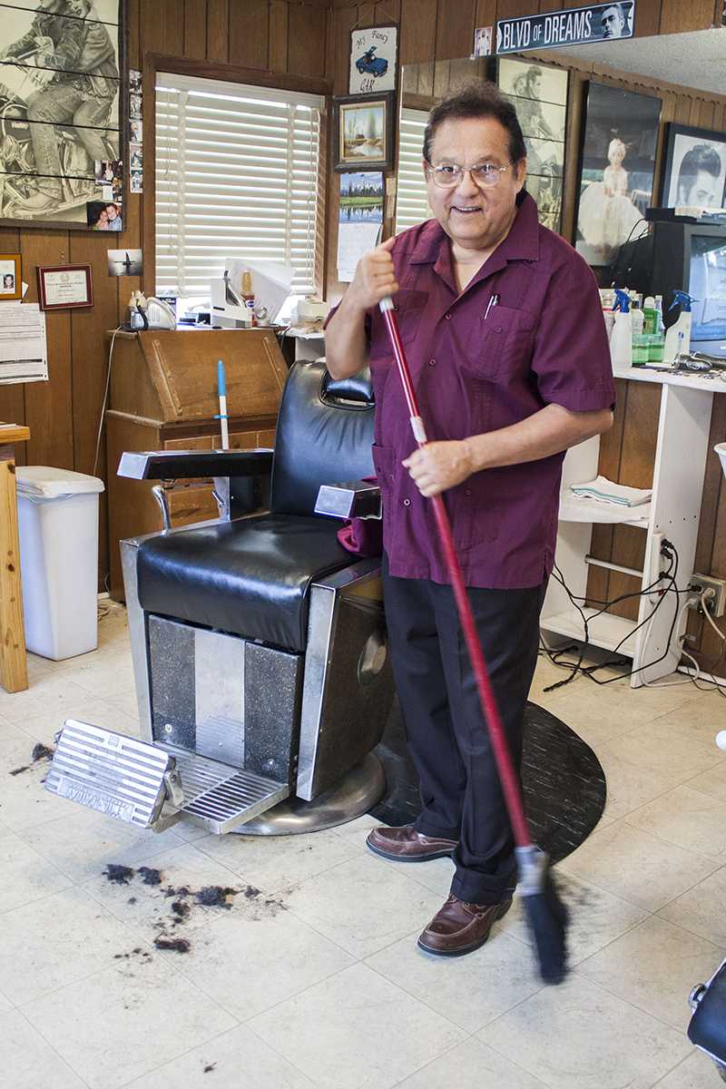 Barbershop owner and operator Lionel Garcia poses while cleaning up his shop.