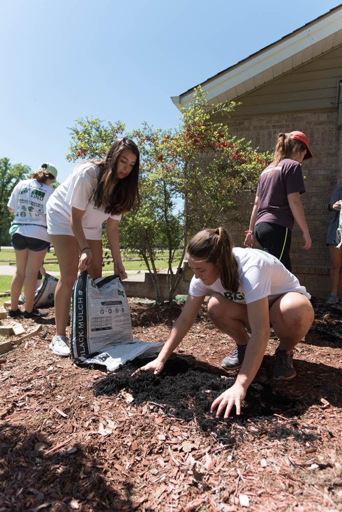 Ana Pozas Garza pours a bag of mulch out as freshman interdisciplinary&#160;studies major Katie Mascari spreads it out.