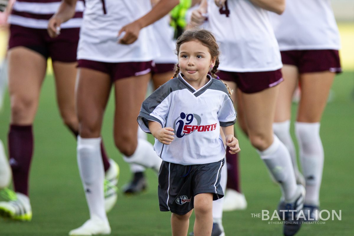 A little girl runs off of the field in front of the Aggie soccer team.