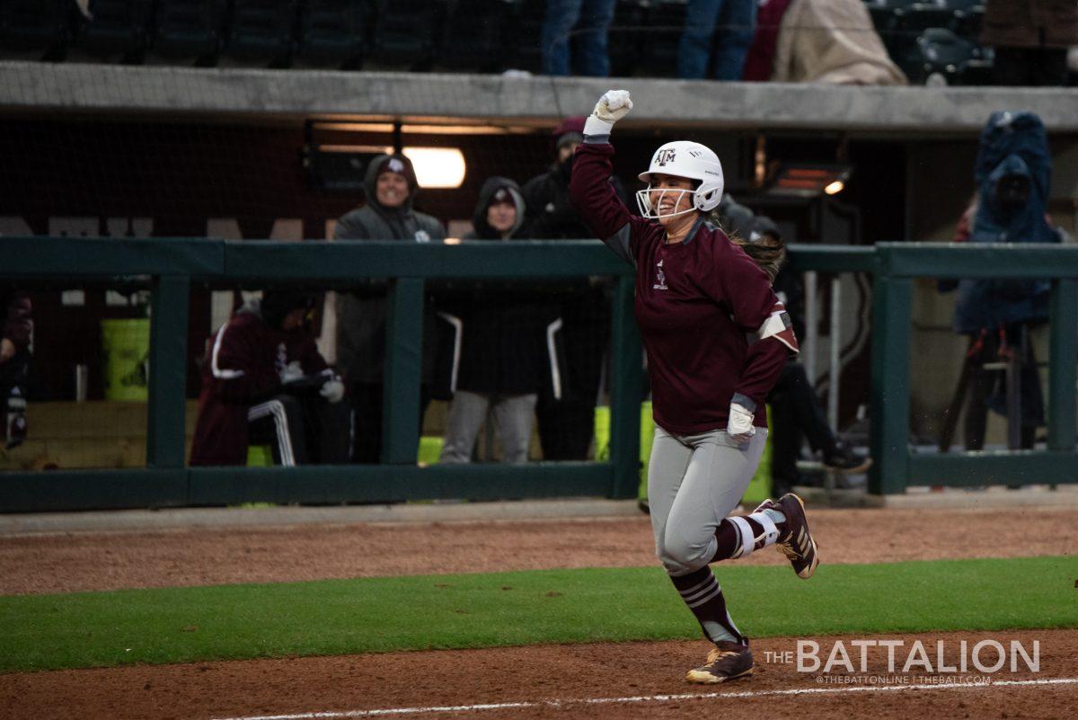 Riley Sartain throws her arms up in the air as she runs down the final stretch to home plate.