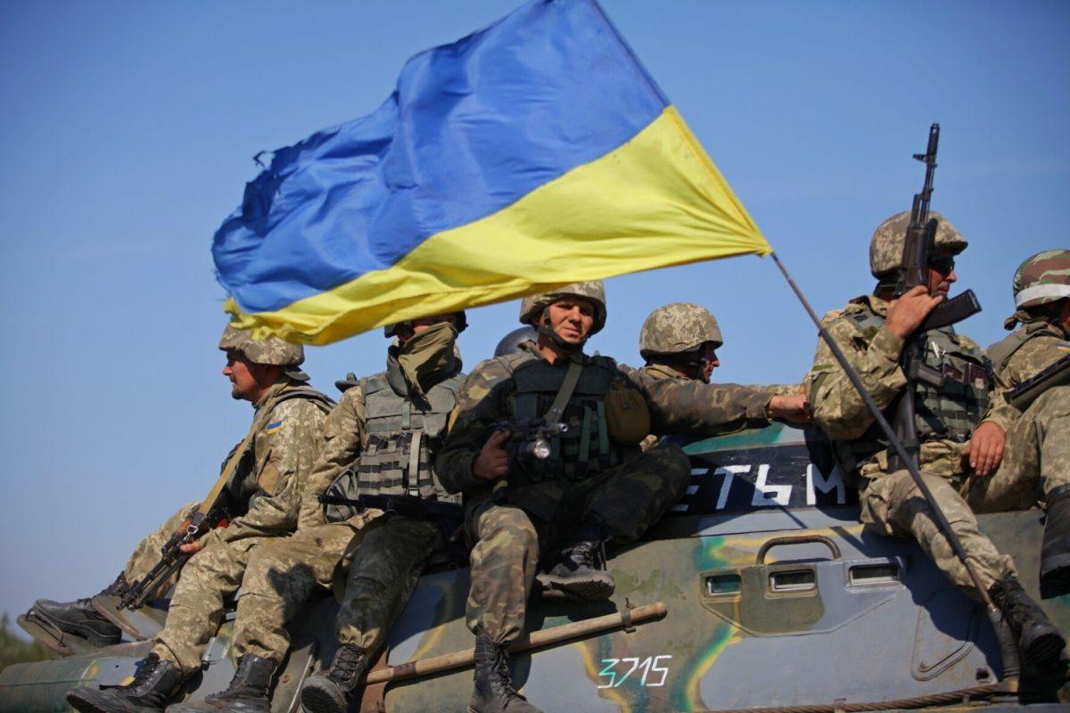 Ukrainian soldiers ride on top of an armored fighting vehicle.