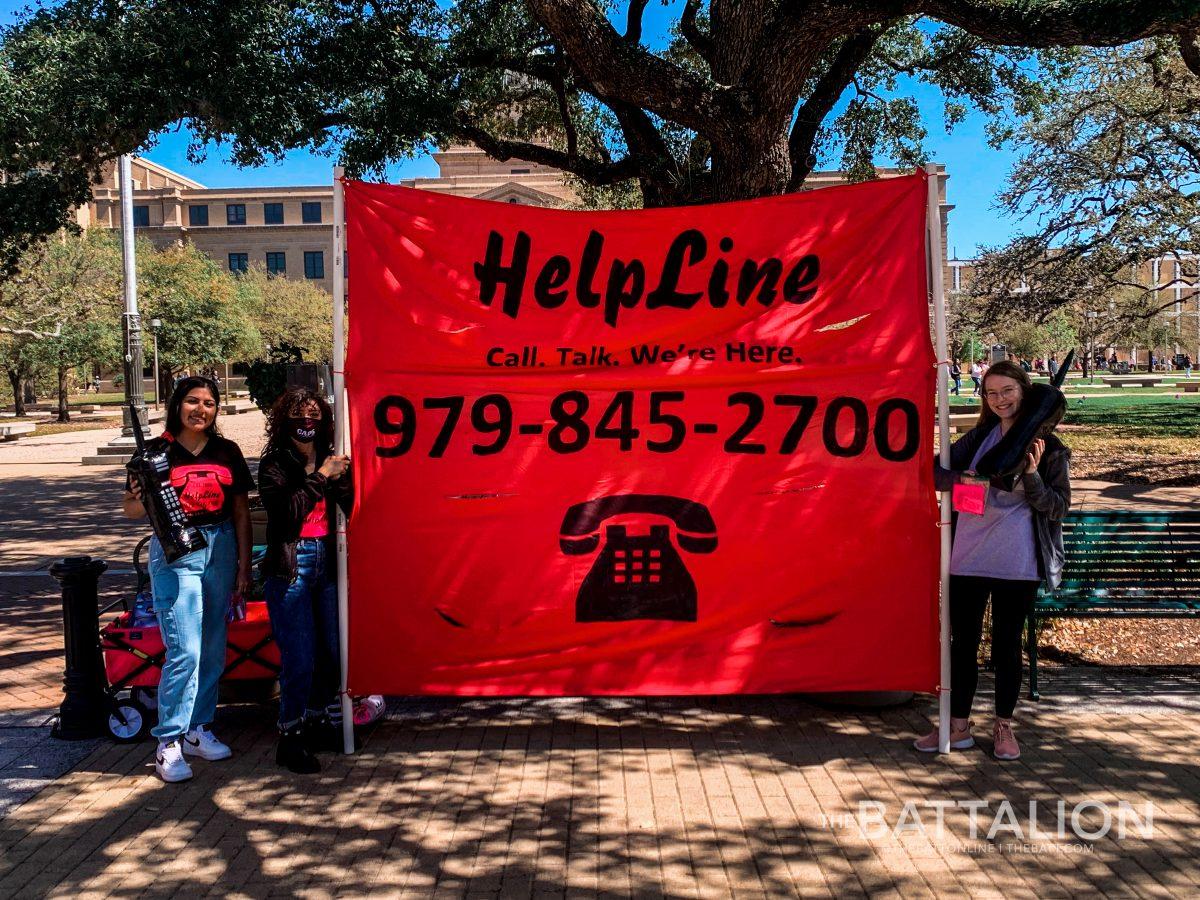 Aggies working with the student HelpLine desk hold up a poster by the Academic building to raise awareness about the organization.