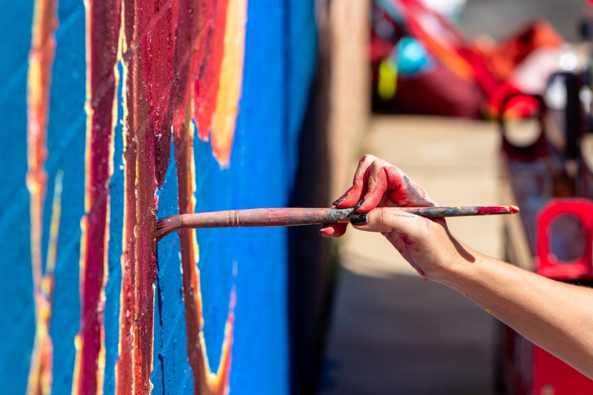 Naomi Haverland paints part of a flower in her mural at University Flowers on Texas Avenue as part of Rev Up The Arts Mural Festival on Wednesday, Oct. 18, 2023. (Photo by Karis Olson/The Battalion)