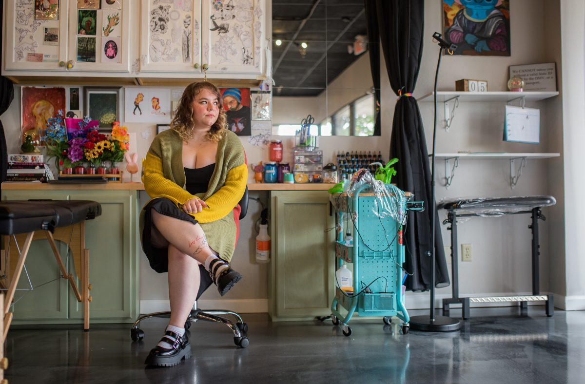 Heather Stalter sits for a photo in front of her work station filled with walls of her art at Sacred Sisters Tattoo Parlor. 