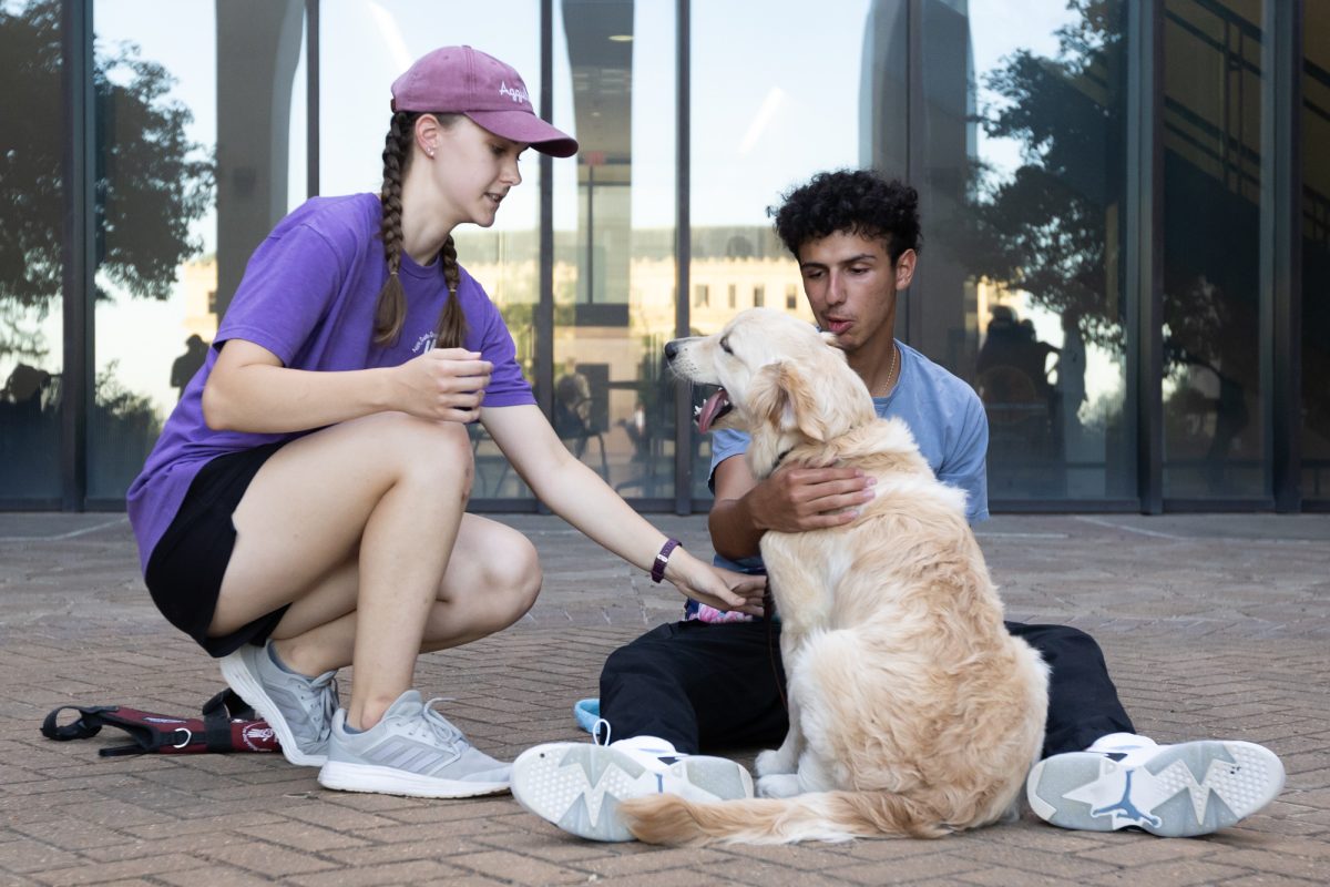 Animal science senior and dog sitter Brooke Brenham instructs general engineering sophomore Antonio Liuzzi while Brenham's service dog, Skylar, a Golden Retriever, sits in Liuzzi's lap during a weekly Aggie Guide-Dogs and Service-Dogs group training session outside the Liberal Arts Building on Monday, Sept. 9, 2024. (Chris Swann/The Battalion)