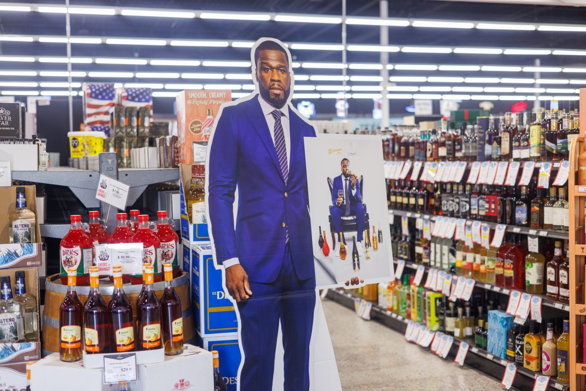 A cutout of 50 Cent holds a photo of the rapper surrounded by bottles of Branson while smoking a cigar inside Spec's in College Station during his signing event on Wednesday, Oct. 2, 2024. (Samuel Falade/The Battalion)