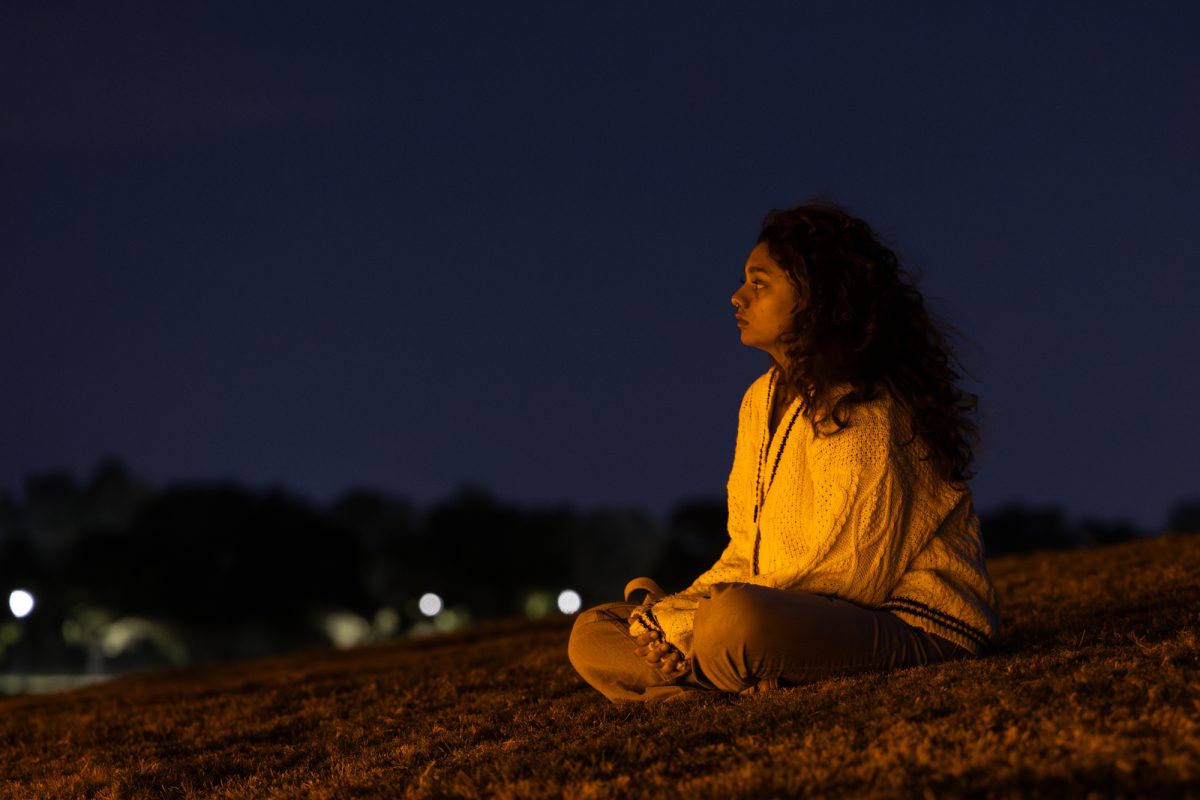 Biomedical sciences junior Mireille Pereira sits on the brim overlooking the memorial after the Bonfire Remembrance Ceremony at the Bonfire Memorial on Monday, Nov. 18, 2024. 